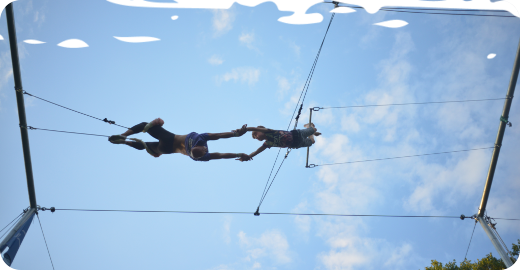 A man is catching a boy doing a trick on a flying trapeze